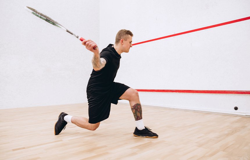 Мужчина в черном спортивном костюме с ракеткой в руках играет в сквош